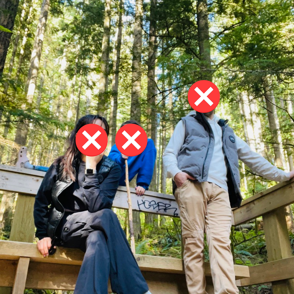 Three people in a forest, sitting and standing on a wooden bench. One holds a hiking stick. Sunlight filters through green trees.