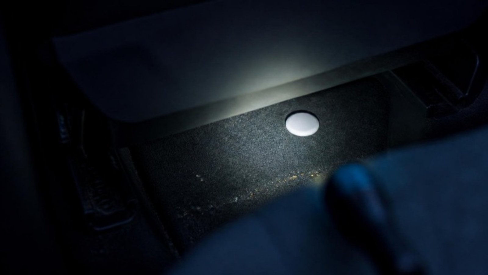 AirTag escondido: localizador Bluetooth debaixo do banco do carro iluminado por uma lanterna