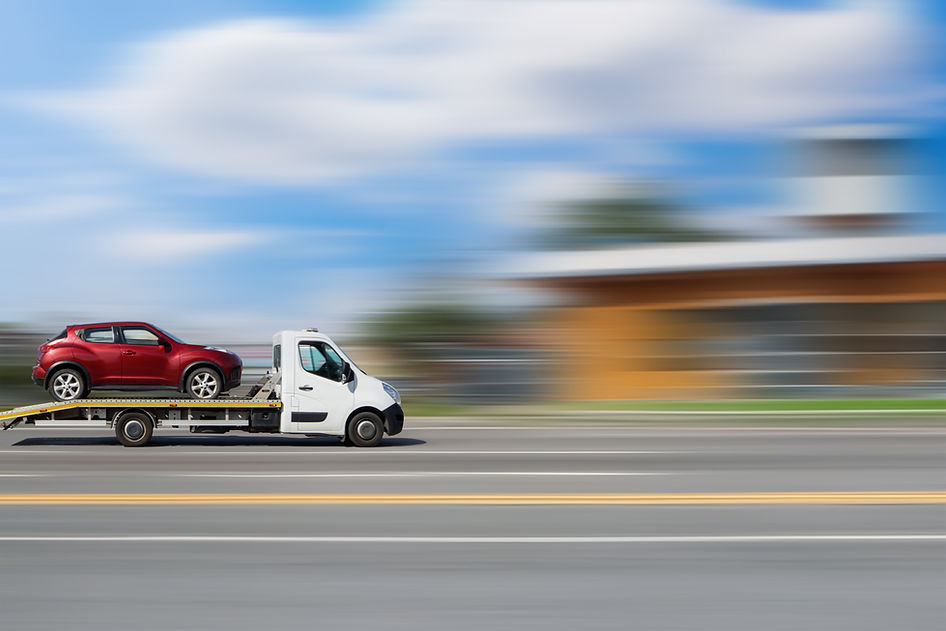 A tow truck is transporting a car. Side view of a moving tow truck transporting a car on a