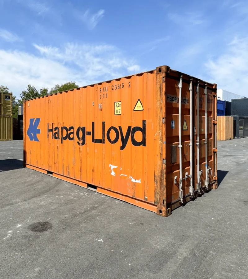 Conteneur orange Hapag-Lloyd avec Container 20 Pieds Dry d’Occasion, sous un ciel bleu.