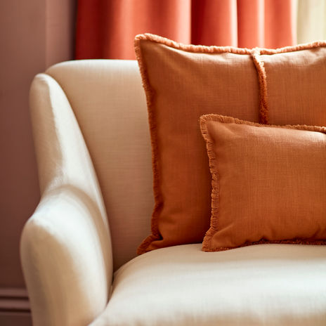 beige möbeltyg på en soffa med roströda kuddar och gardin i orange