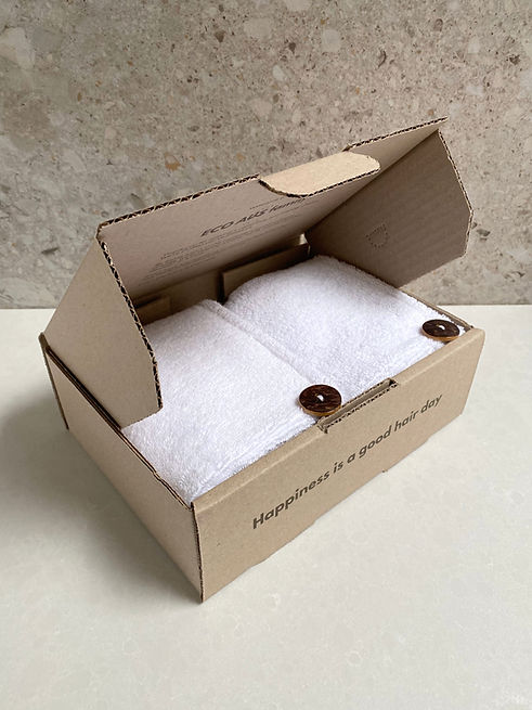 Eco-friendly box with two white hair towels featuring natural buttons and the text 'Happiness is a good hair day'