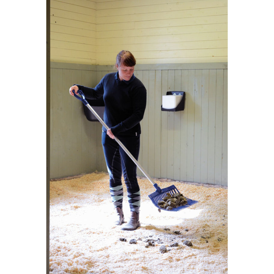 Une personne balayant le sol. La personne est dans une écurie, avec une pelle.