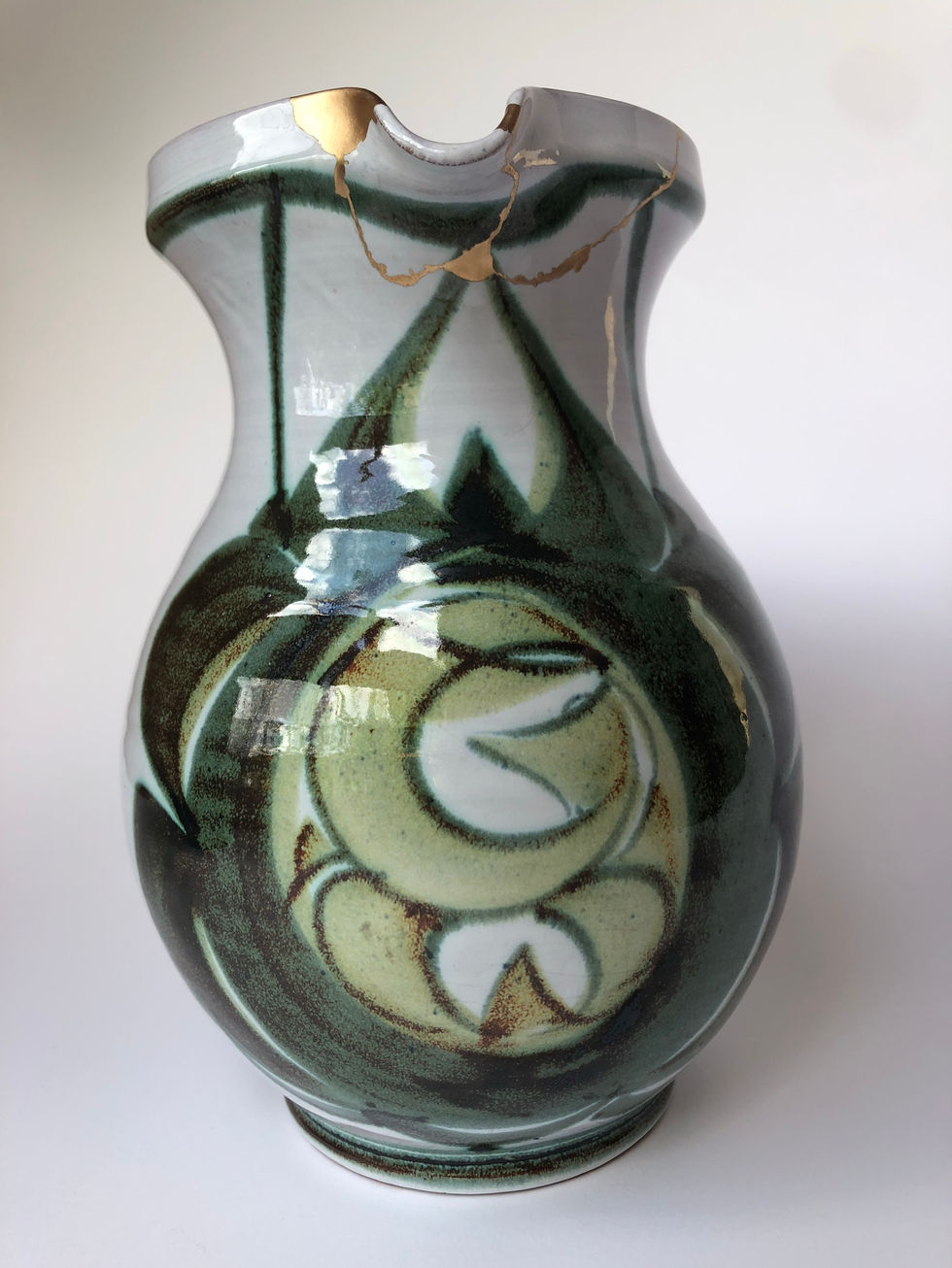 Kintsugi art. The break lines and missing areas of a broken green and grey jug are finished with a striking gold-hued brass.
