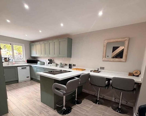 Modern open plan kitchen and dining area fitted with green cabinets and breakfast bar stools