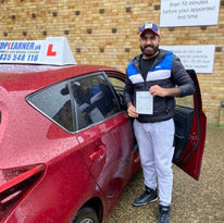 Male student holding driving test pass certificate next to red car