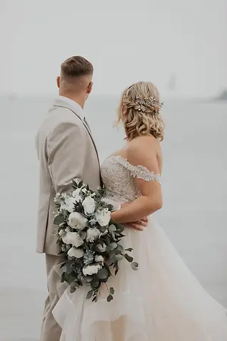 Bride and groom standing together while holding a large white rose and eucalyptus bouquet
