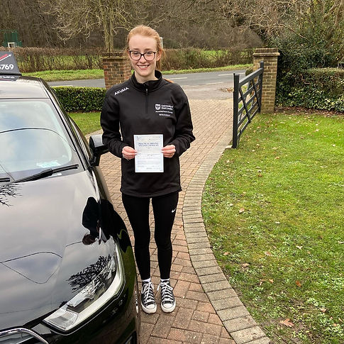 Happy female student standing in front of a tuition car holding her practical driving test certificate