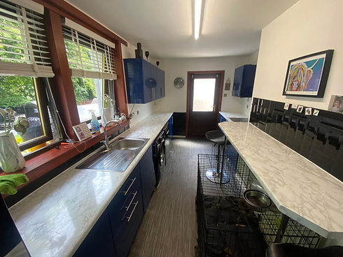 Long galley kitchen featuring deep blue vinyl wrapped units and white marble effect worktops