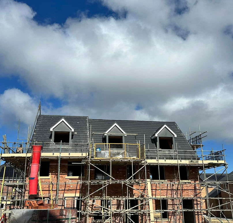 A brick house under construction with scaffolding, set against a blue sky with fluffy clouds