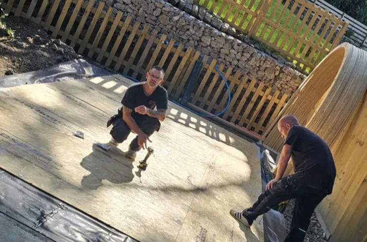 Two tradesmen installing floor insulation on a timber hut base outdoors
