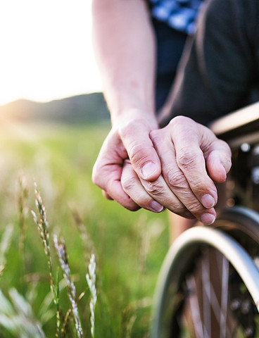 Detail shot of a carer’s hand resting supportively on the hand of a person in a wheelchair