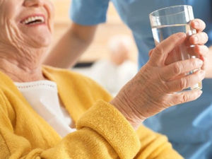 An elderly woman laughing as a caregiver hands her a glass of water
