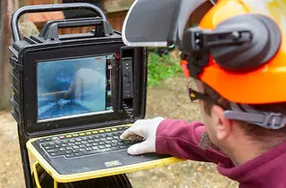 Drainage technician operating a CCTV camera inspection monitor outdoors