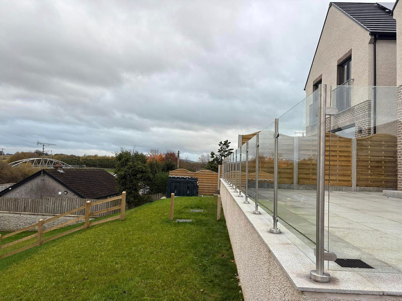 A modern house with a glass balcony overlooks a grassy yard