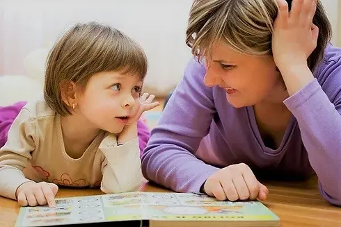 A nursery worker smiling and reading a book with a young toddler girl