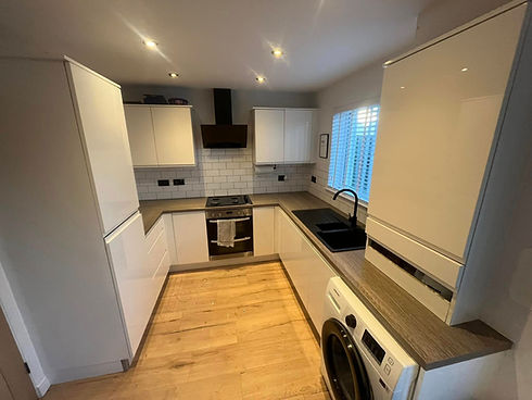 Completed kitchen renovation featuring glossy white cabinets and natural wood flooring