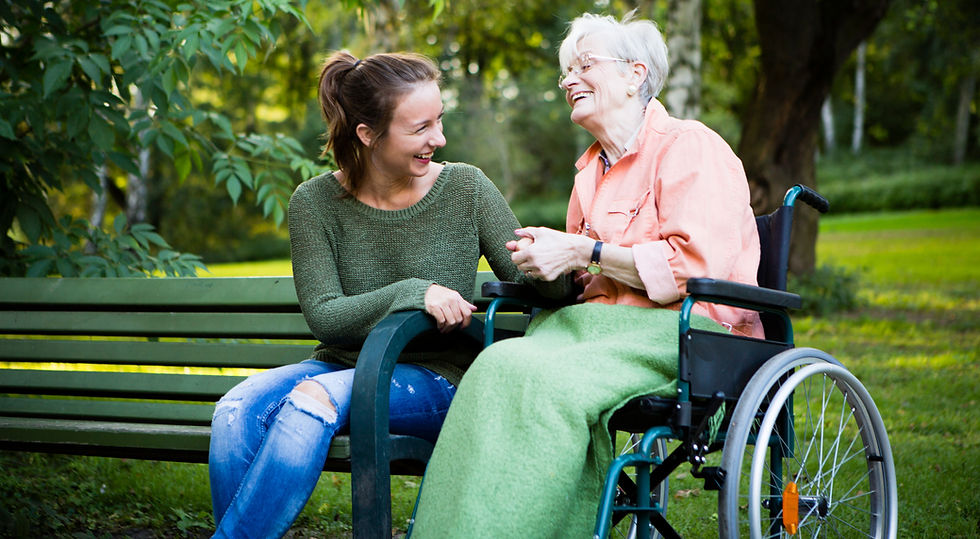 Friendly carer chatting with a senior woman in a wheelchair outdoors in a park