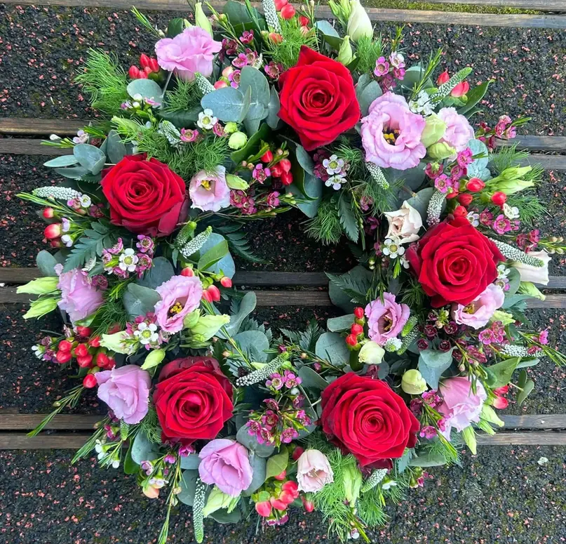 Traditional circular funeral wreath featuring deep red roses and pink lisianthus with mixed greenery