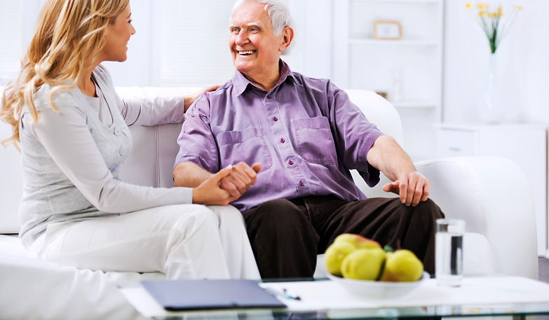 Smiling blonde woman chatting with an elderly man sitting on a living room sofa