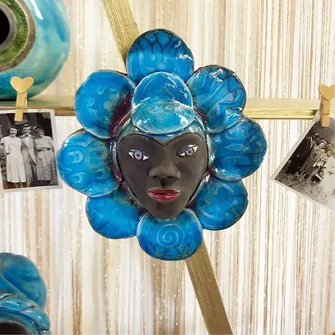 Close up of a blue flower shaped ceramic wall hanging with a face