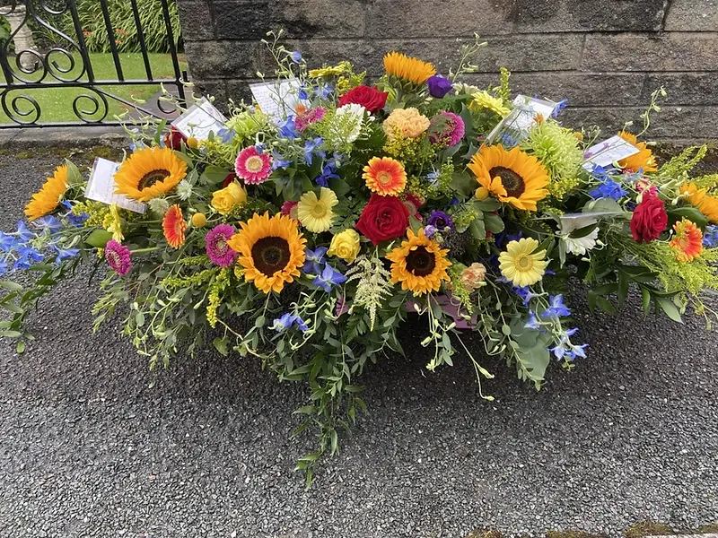 Large funeral tribute featuring bright yellow sunflowers and orange gerberas