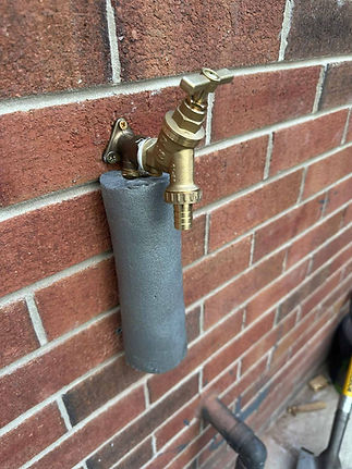 Brass outdoor garden tap installed on a red brick wall with grey pipe lagging