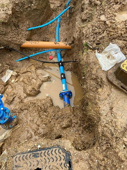 Blue water pipe joint with a bolted flange connection resting in a wet mud excavation pit