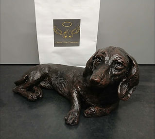 Metallic dog urn sculpture beside a white branded presentation bag