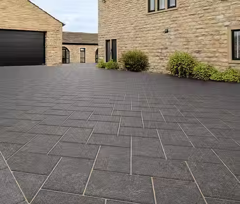 Clean dark grey block paved driveway leading towards a stone building exterior