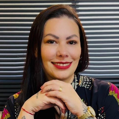 Mulher sentada com as mãos cruzadas, olhando para a câmera.