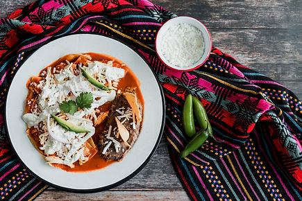 Mexican chilaquiles food with spicy red sauce, chicken and avocado traditional breakfast i