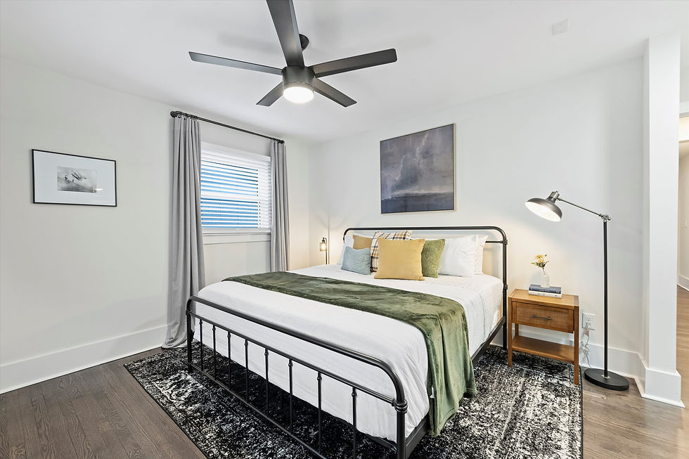 Bright modern bedroom with black metal bed, green throw, wall art, ceiling fan, floor lamp, and gray curtains over a window.
