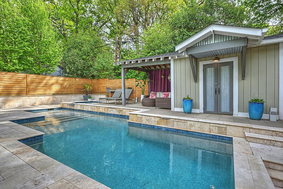 Outdoor pool with clear water, surrounded by tan stone tiles. Nearby, a cozy seating area under a wooden pergola, and lush greenery.