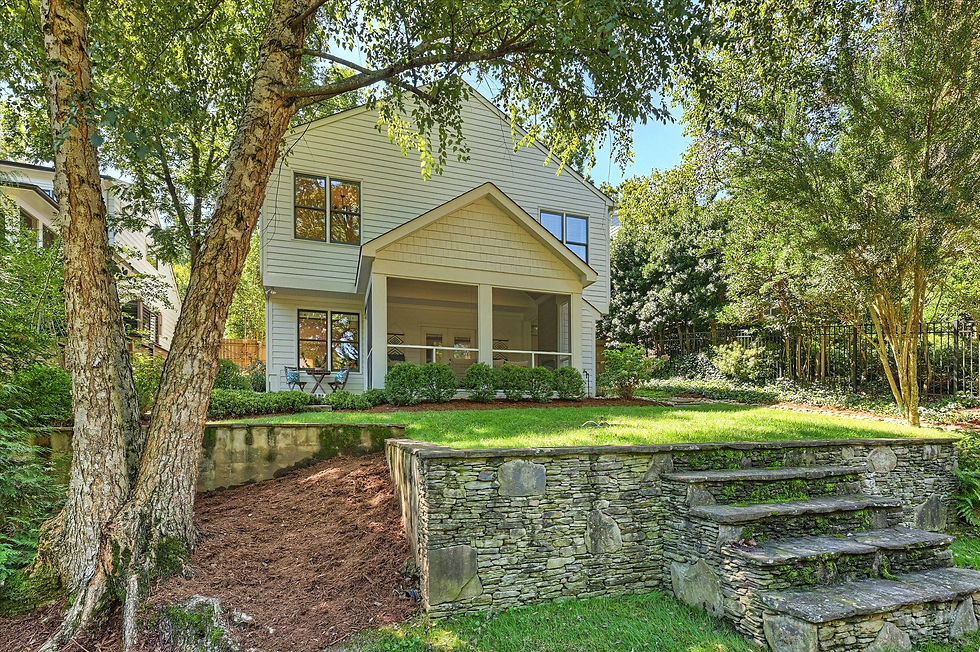 Sunny backyard with a white two-story house, stone steps, green lawn, and leafy trees casting shade