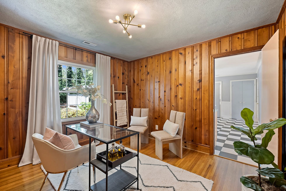 Cozy wood-paneled sitting room with beige chairs, glass table, white rug, window curtains, and open doorway to a checkered hall.