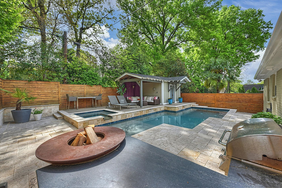 Backyard with a pool, wood deck, fire pit, and grill. Chairs and a table are near a small cabana. Surrounded by a wooden fence and trees.