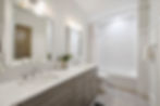 Modern bathroom with dual sinks on a marble countertop, large mirrors, and a shower with a white curtain. Bright lighting and a tidy ambiance.