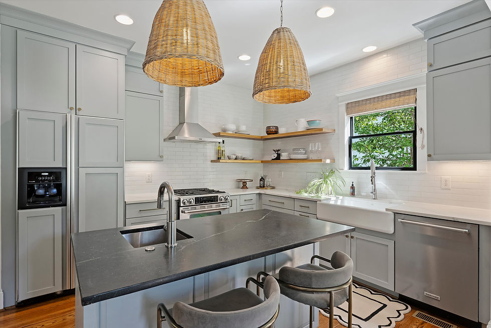 Bright modern kitchen with gray cabinets, black island, wicker pendant lights, open shelves, farmhouse sink, and green view outside.
