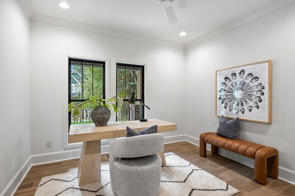 Modern office with a wooden desk, gray chair, and black lamp. Large windows, abstract art on the wall, and a brown bench with a cushion.
