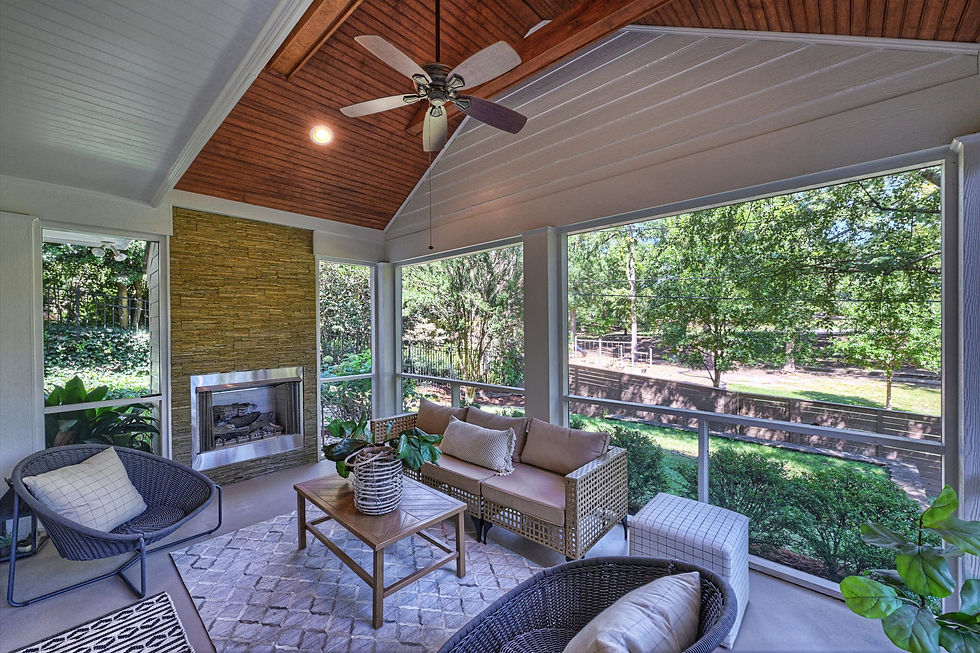 Bright screened porch with wicker seating, fireplace, and ceiling fan overlooking a leafy backyard.