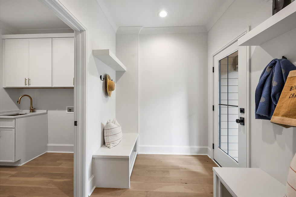 Bright mudroom with a bench, beige hat on a hook, and a striped pillow. White cabinets in background, blue cloth and bag hang by door.