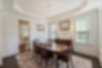 Elegant dining room with dark wood table and chairs, gold chandelier, white walls, large windows, and framed mirror and art