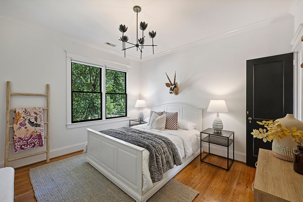 Bright modern bedroom with white bed, black lamps, antelope wall art, patterned throw, and green trees visible through windows.