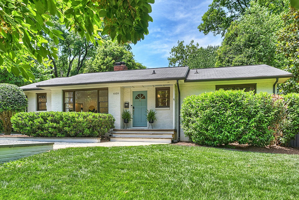 A cozy white house with a light blue door, flanked by green bushes and trees. A well-maintained lawn is in the foreground under a blue sky.