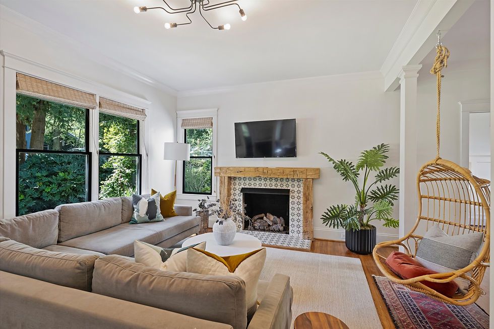 Bright modern living room with gray sectional, fireplace, wall TV, hanging wicker chair, and green plants by large windows