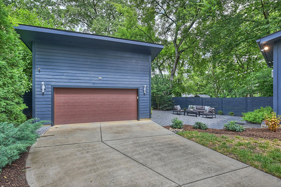 Modern blue garage with wood door beside a gravel patio seating area under trees and string lights.