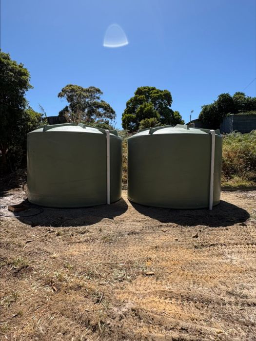 Two green rainwater tanks on a cleared site