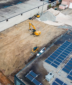 Aerial view of a construction site being prepared by Peninsula Excavation, showing heavy machinery in action, including an excavator, and solar panels on the building's roof.