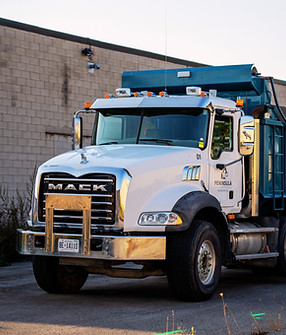 Peninsula Excavation's Mack dump truck parked at a construction site, featuring a large blue dump trailer and company branding visible on the truck’s side.